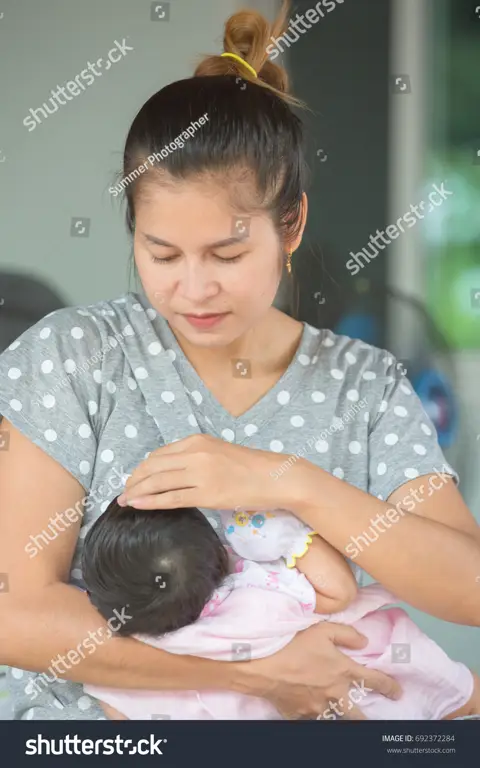 Seorang ibu menyusui yang terlihat bahagia dan tenang.