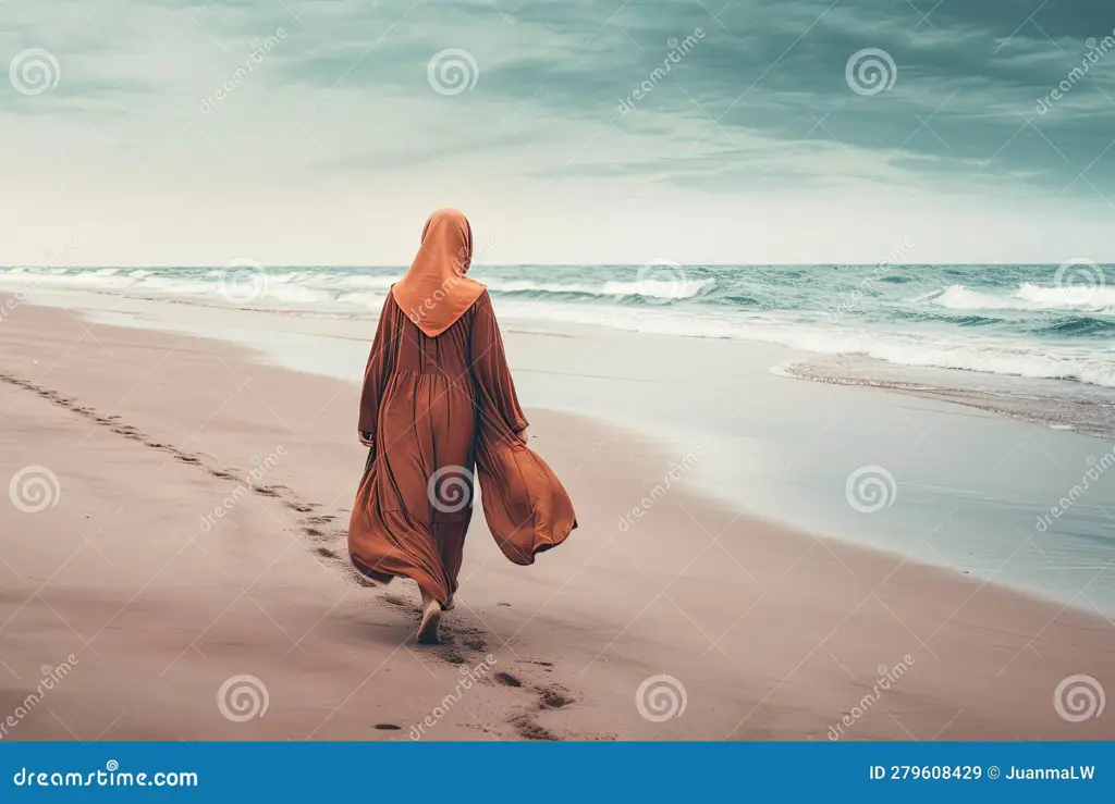 Wanita berhijab berjalan di pantai saat matahari terbenam