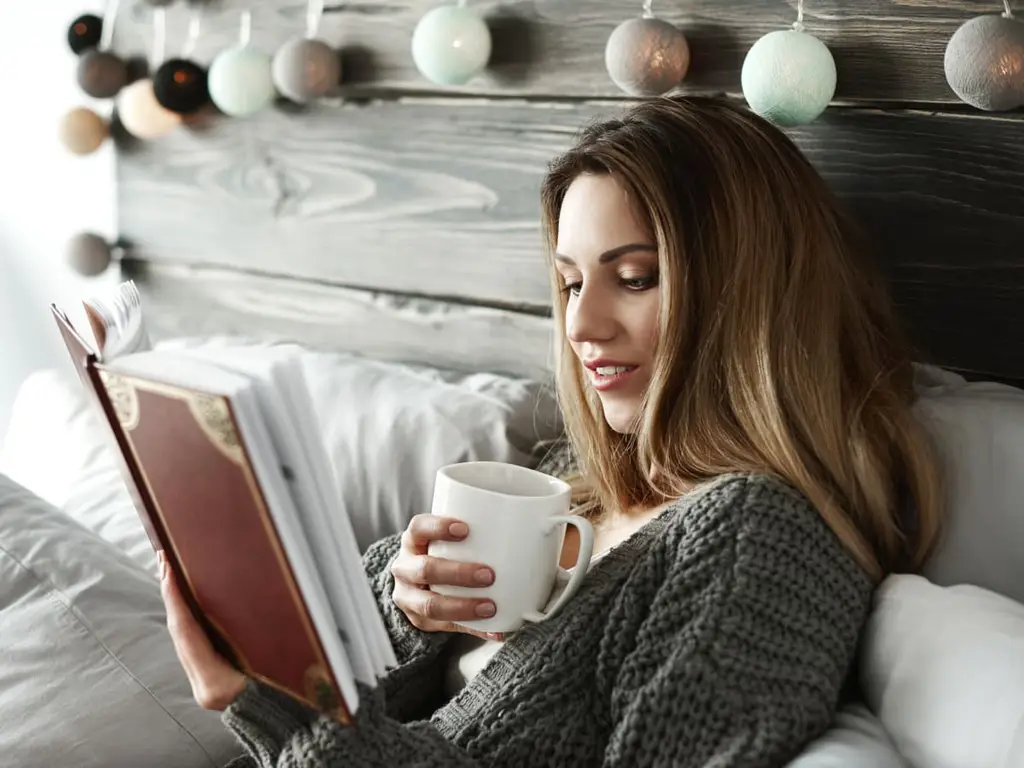 Gambar seorang wanita membaca buku di tempat tidur