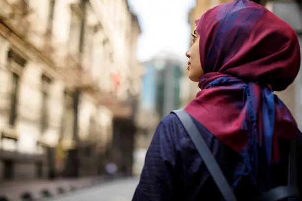 Gambar wanita berhijab berjalan dari belakang di tengah kota yang ramai.